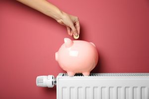 putting money into a pink piggy bank sat on top of a radiator